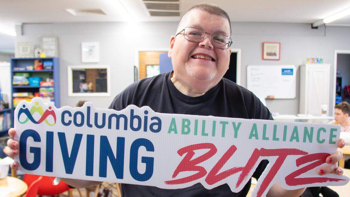A Columbia Ability Alliance client, Kelly Morris, proudly holds up a sign while preparing for the 2025 Giving Blitz.