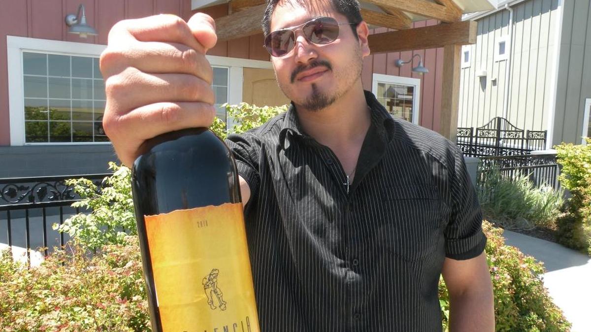 Victor Palencia holds a bottle of his Palencia Wine Co. in front of his Walla Walla winery. The drawing on the label depicts his father with a shovel as he works the fields of the Yakima Valley.
