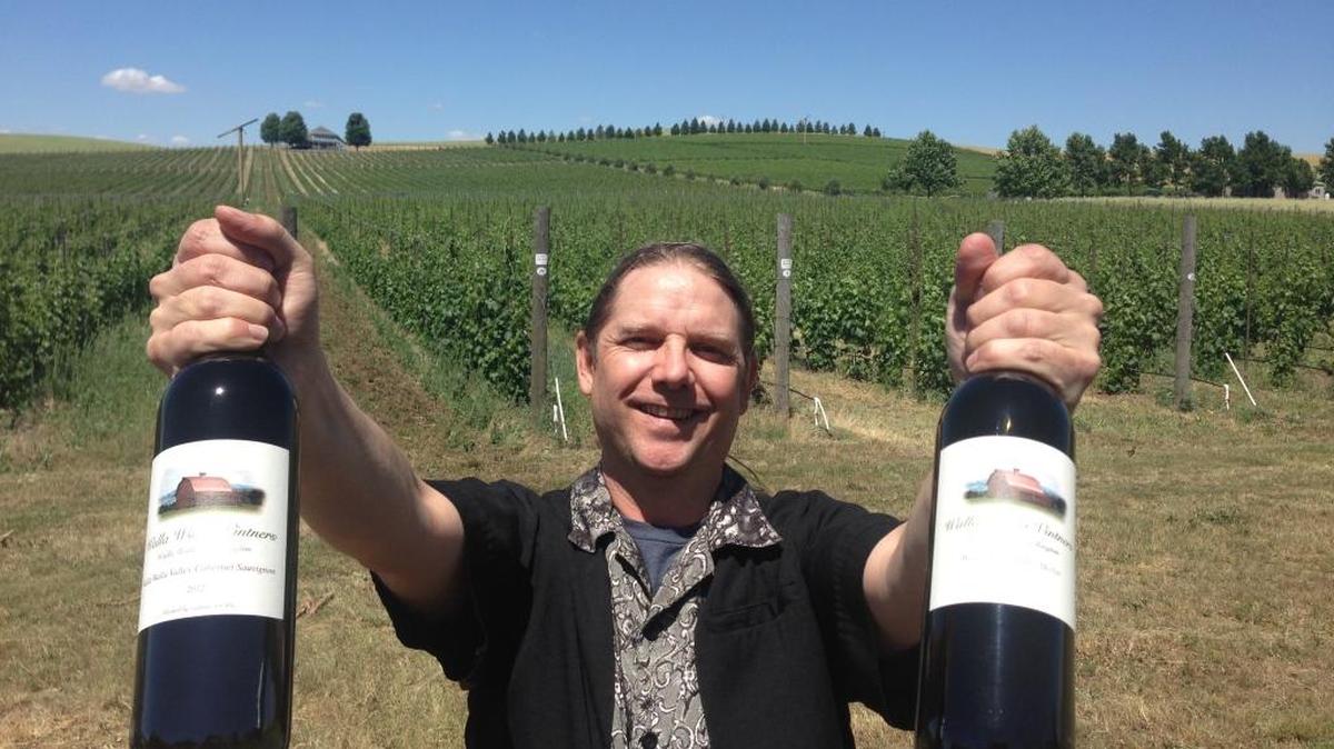William VonMetzger, winemaker for Walla Walla Vintners, holds up two bottles of his award-winning wines in front of the winery’s estate vineyard east of Walla Walla.