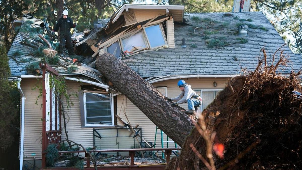 Jake Hines, left, and Ross Rukke, of Capstone Construction, work to remove a fallen tree in Spokane after deadly storms swept through the state leaving many without power.