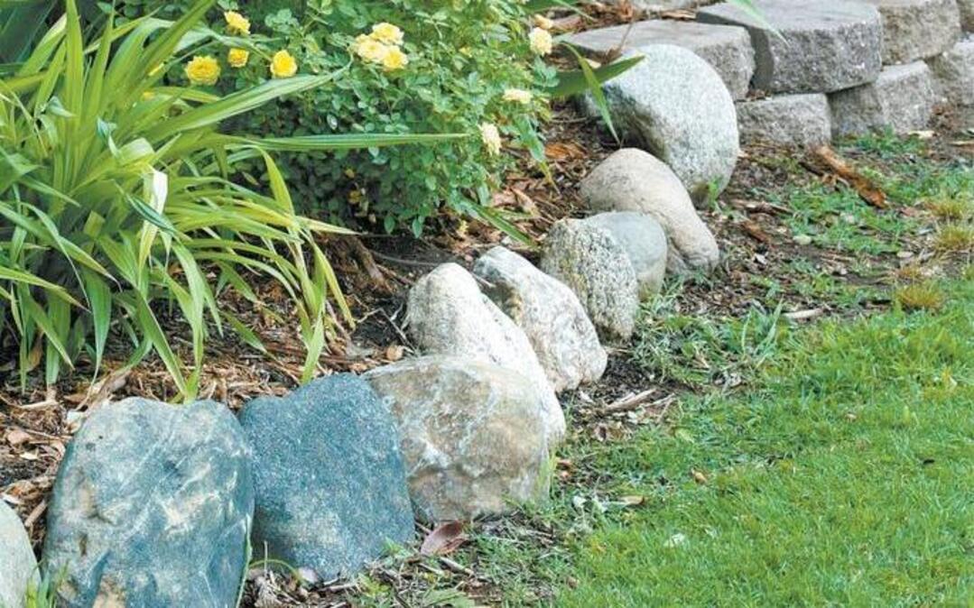 Rocks (foreground) and decorative concrete blocks form the border along the edge of the large yard. Quality landscape edging makes it easier to mow along lawn edges, to keep grass from creeping into flower shrub beds, and to contain mulching materials.