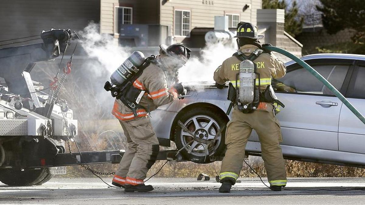 Kennewick firefighters work to extinguish a fire in the engine compartment of a 2005 Mitsubishi sedan that was being towed to a repair shop when it caught fire on Highway 395 at West 27th Avenue in Kennewick.