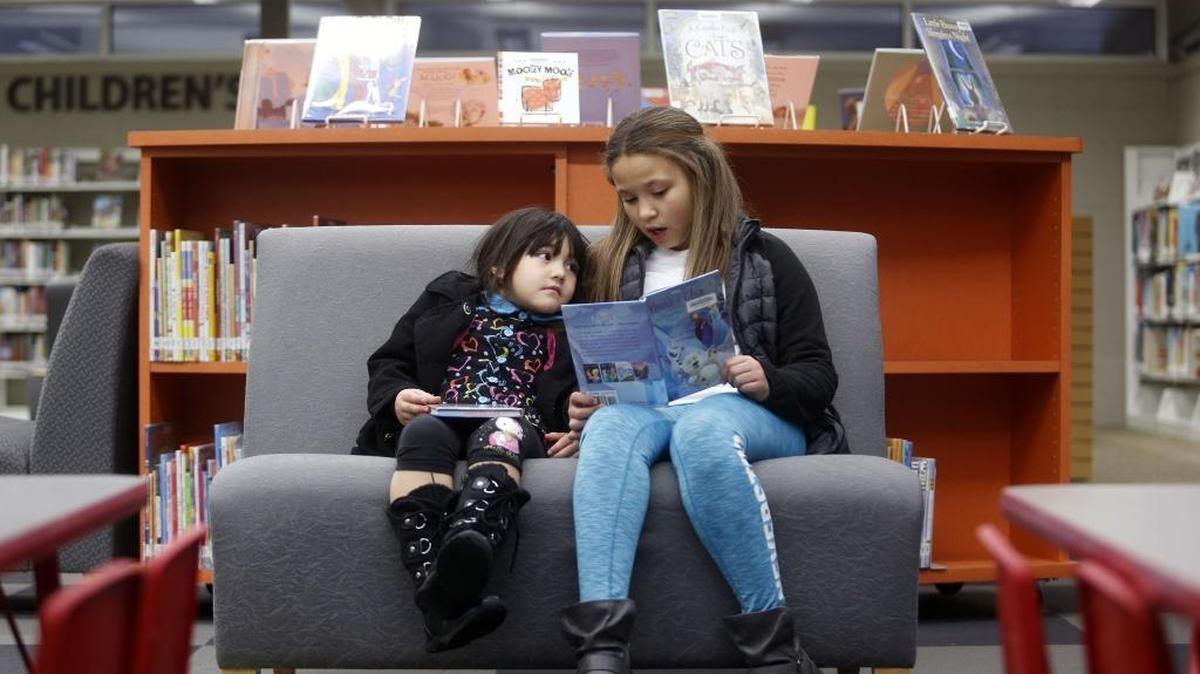 Jade Williams, right, 10, of Oregon, reads Anna & Elsa; the Polar Bear Piper, to family member Markirie McKinnis, 4, of Pasco, on Tuesday at the Mid-Columbia Libraries branch in Pasco. Library officials plan to talk with Pasco, West Richland, Prosser and Kahlotus about being annexed by Mid-Columbia Libraries rather than just contracting for library services.