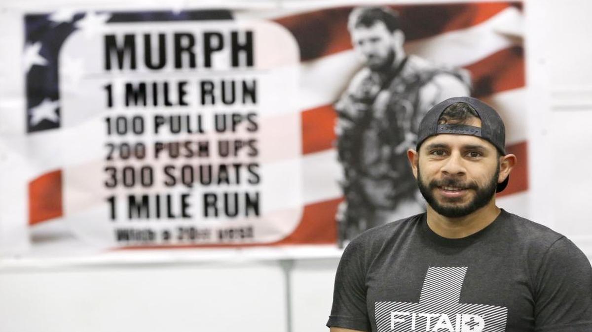 Leo Barillas, owner of Natural Selection CrossFit, stands near a poster in the Kennewick gym describing the workout event on Memorial Day to raise money for the Wounded Warrior Project.