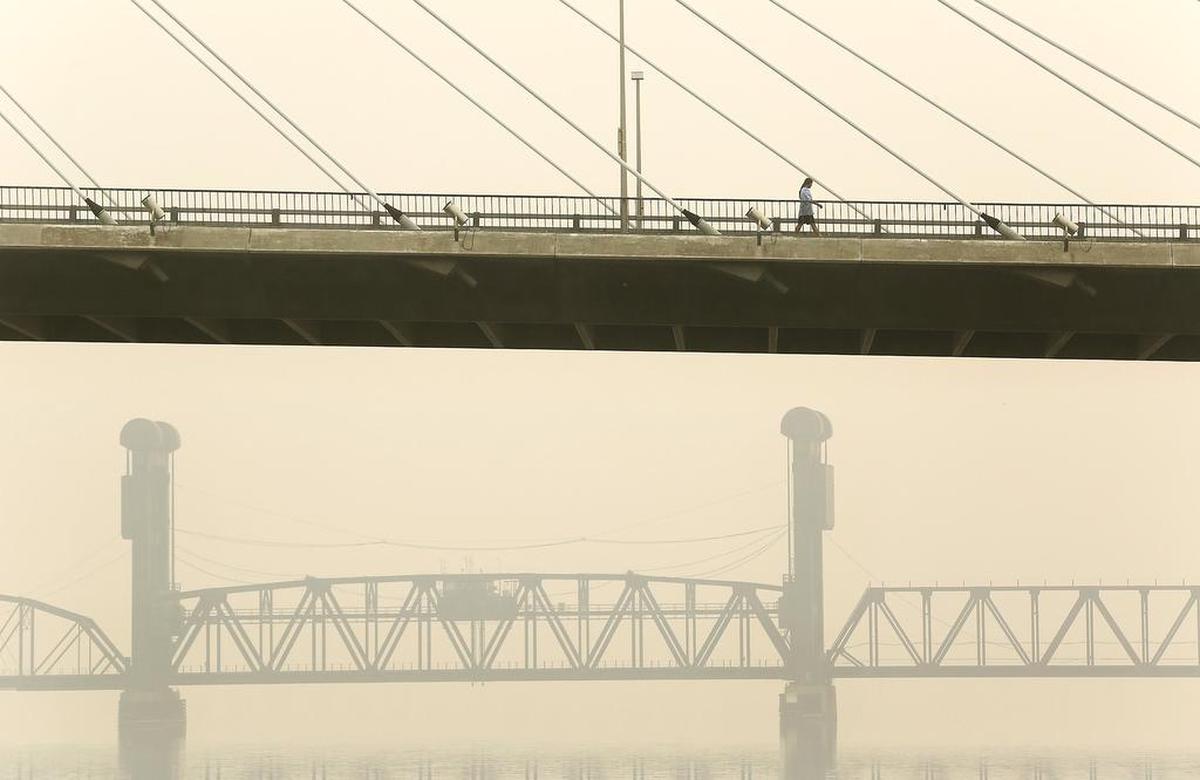 A pedestrian strides across the cable bridge in 2017 with a hazy and smoke-filled backdrop on the Kennewick side of of the Columbia River.