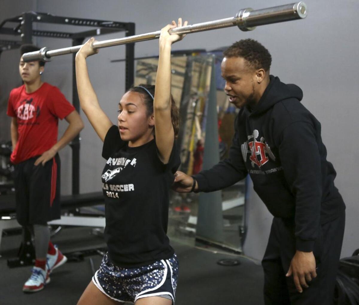 Steven Whitehead helps Justice Aragon, a senior at Chiawana High School, with her form while doing a squat during a early morning training session with high school athletes at Elite Ambitions Training in Kennewick. Whitehead, founder and owner of E.A.T., runs multiple training classes for high school athletes.