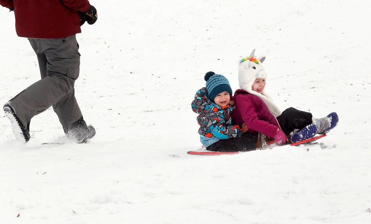 William Winsley, 22 months, and his 5-year-old sister, Maria, wear big grins as they slide down the snowy hill at Carmichael Middle School in Richland. Their father, Justin Winsley, of Kennewick, jogs beside the sled during their ride.