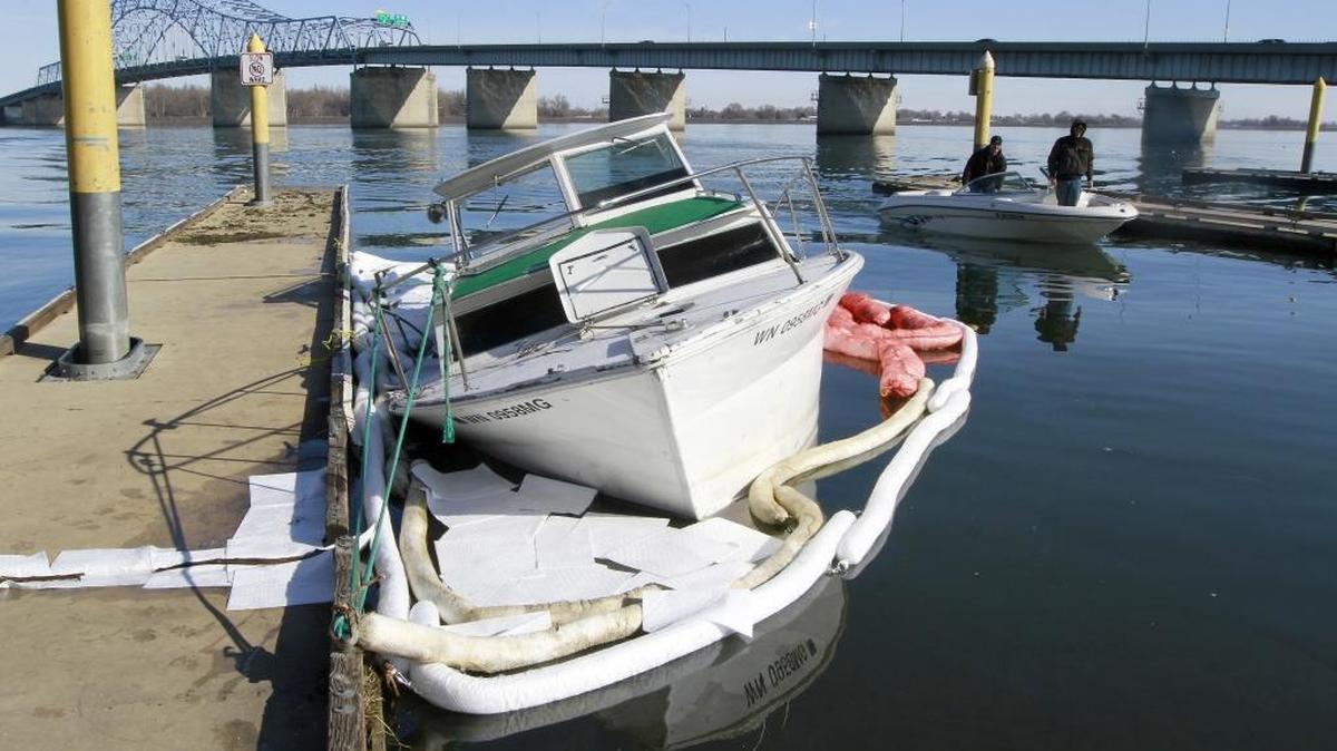 The partially submerged 1963 Fairliner owned by Dave Ladomirako is surrounded by oil and gas containment materials Monday at the docks of the boat launch in the east end of Kennewick’s Columbia Park. A local marine service helped re-float and move the damaged vessel off the rock levee of the Pasco shoreline over the weekend. Ladomirako apparently didn’t have a trailer to haul away the 28-foot boat damaged by ice a week ago.