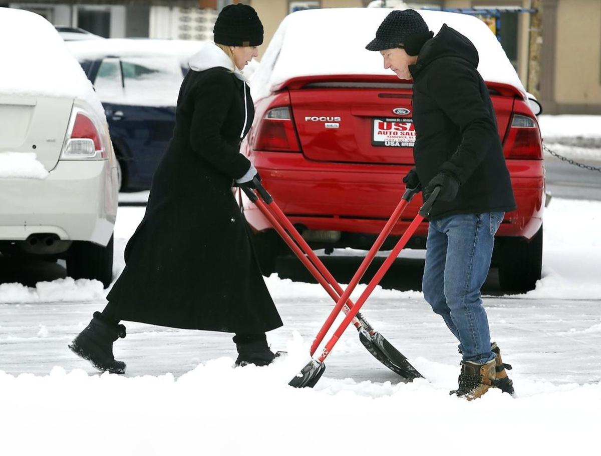 Rhonda and Darryl Coffin, owners of USA Auto Sales, double-team their snow removal efforts Tuesday morning from the parking lot of their Kennewick automobile sales business on Columbia Drive in Kennewick. The two were each holding a pair of snow shovels while they clear the recent light and dry snowfall.