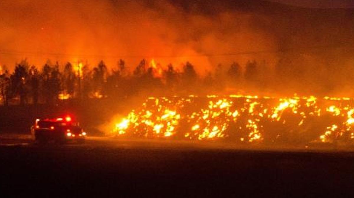 A fire truck moves along Highway 125 past a blazing stack of hay bales north of Walla Walla during a large wildfire Sunday night. Firefighters from several districts were able to stop the blaze at Highway 125. The fire burned about 15,000 acres in high winds and was contained about 11 p.m.