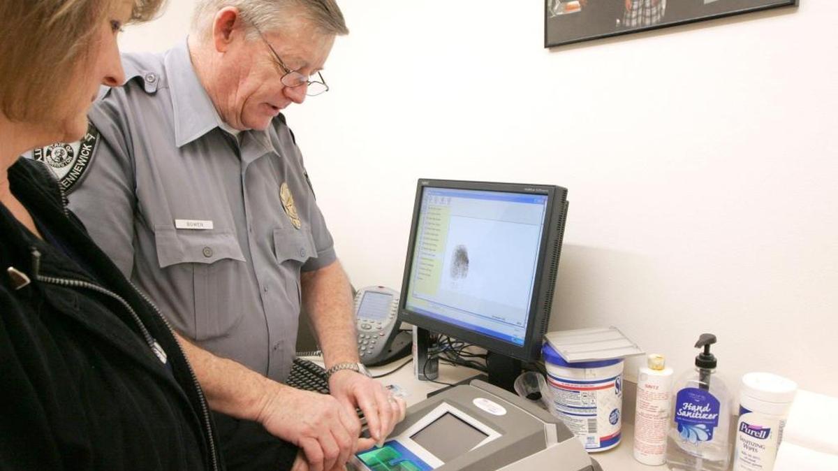 Darlene Agnew of Kennewick has her fingerprints taken in 2013 by Kennewick Police Department technician George Bowen. The procedure is required for all concealed-pistol license applicants. With offices closed due to a COVID exposure, pistol licensing and fingerprinting appointments are being rescheduled by the Benton County Sheriff’s Office.