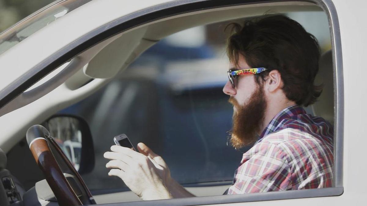 An man works his cellphone as he drives through traffic.