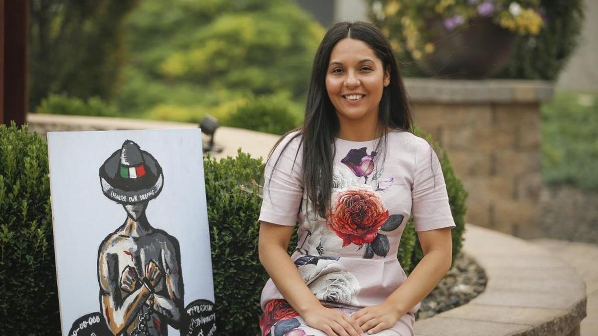 Elizabeth Hernandez, 29, sits outside Columbia Basin College in Pasco on Tuesday next to a painting that she and her brother, Victor, painted about the DACA initiative that shielded young immigrants like her from deportation.