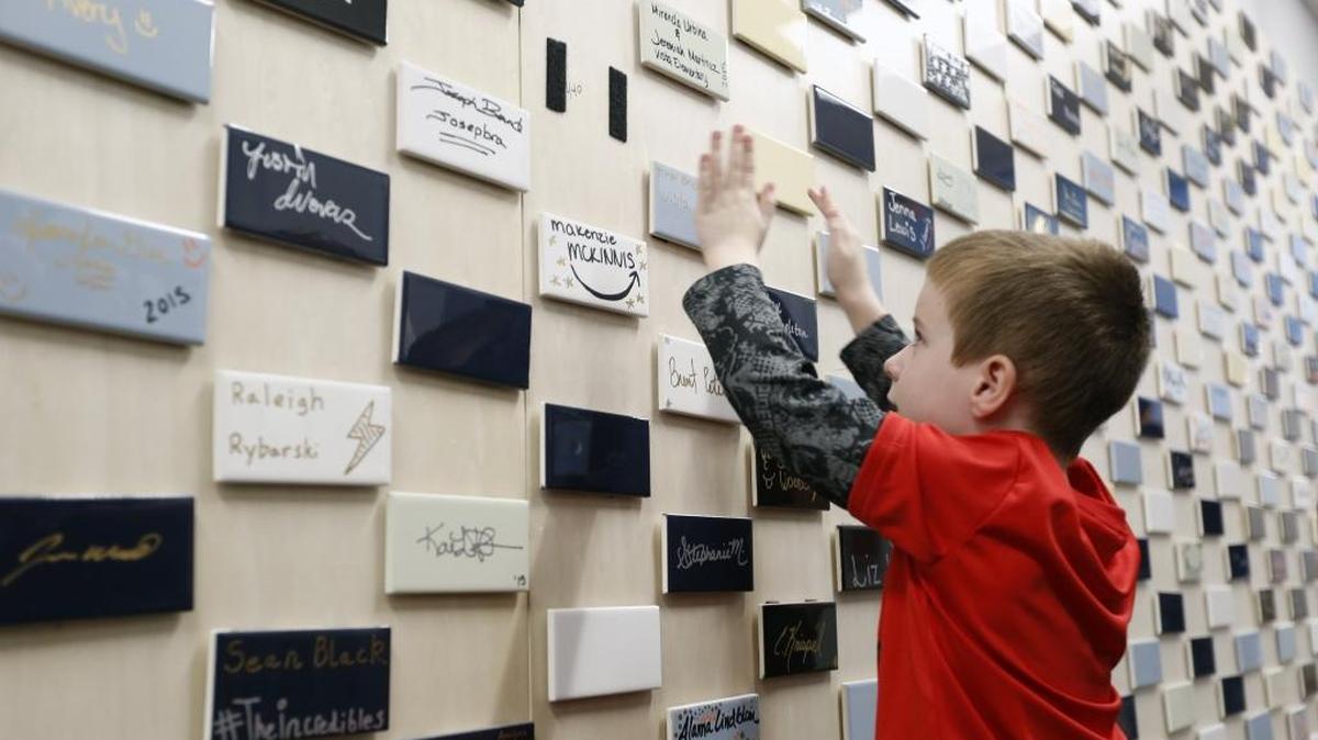 Ira Brickey, a kindergardner at Vista Elementary School, puts up a tile he signed Tuesday during a celebration of the 10th anniversary of the Amazon Customer Service Center in Kennewick. In recognition of the milestone, Amazon presented the school, which many of the company’s employees’ kids attend, with $5,000 worth of school supplies.