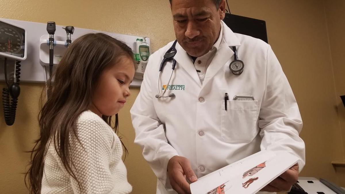 Aryanna Vargas, 4, describes the action in a Curious George book to Dr. Saul Valencia at Pasco’s Tri-Cities Community Health branch.