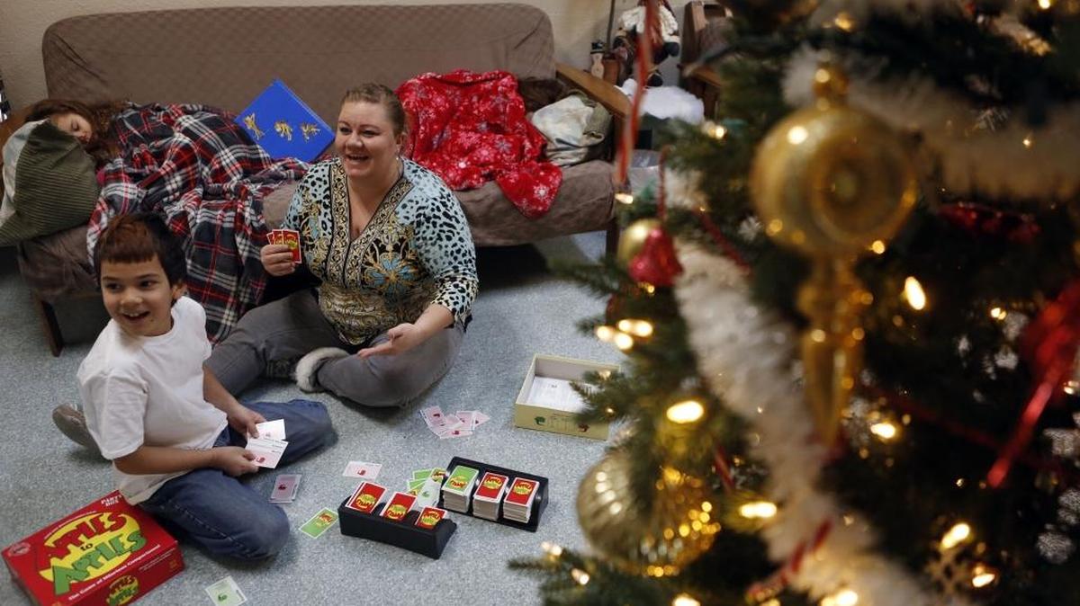 Jessica Rose plays a game of Apples to Apples with her son Tugade Morales, 8, as her 3-year-old twins Delena, right, and Sophia Morales, sleep on the sofa in the community room at the Tri-City Union Gospel Mission’s shelter for women and children in Pasco. Rose has been at the shelter for about two weeks.