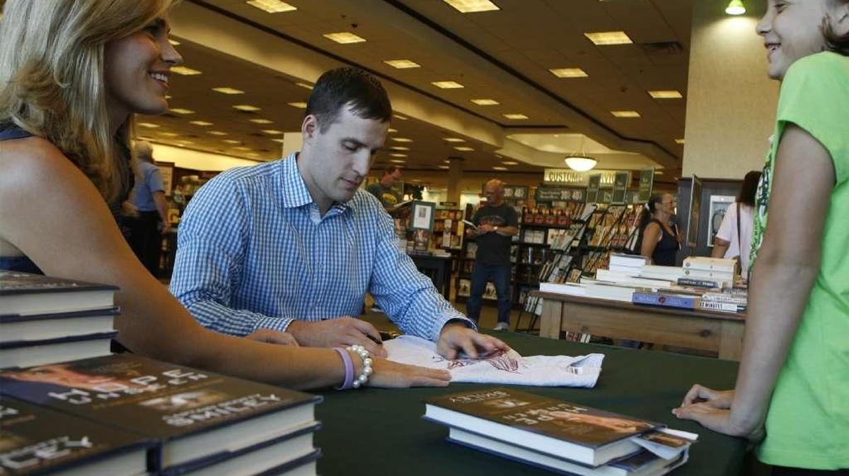 Major Scott Smiley, shown with his wife, Tiffany, signs a t-shirt during a book signing event.
