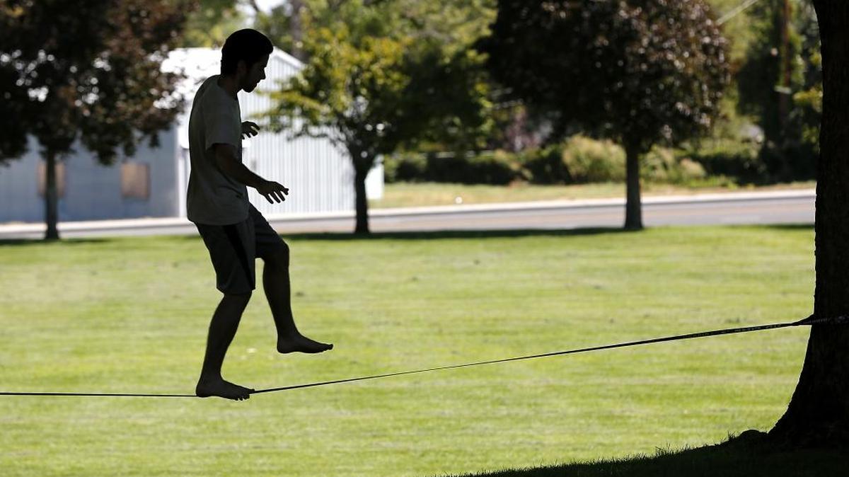 Sam Hart, 19, is silhouetted under the shade trees at Flat Top Community Park in West Richland on Monday while he practices walking across the nylon webbing of a slack line. The Brigham Young University student is home for the summer. Daytime high temperatures are expected to stay in the high 90s all week around the Mid-Columbia.