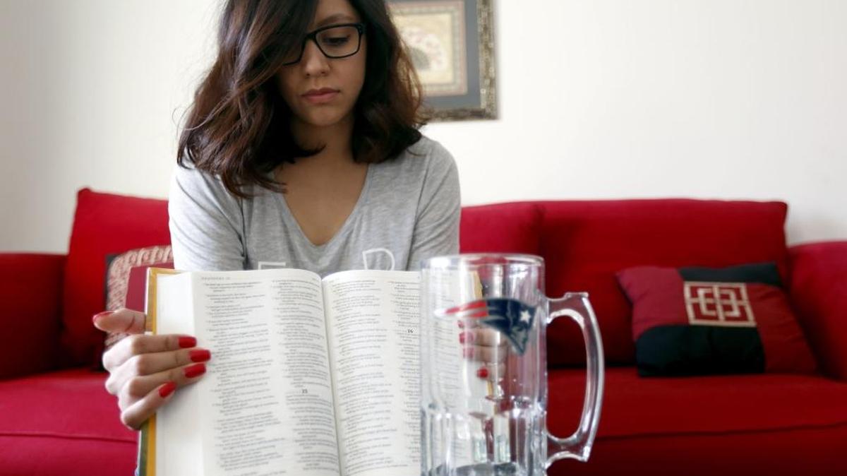 Manuela Medrano, 22, holds open her friend Mannie Aispuro’s Bible to Chapter 25 of the Book of Proverbs, which he was reading the night before his death, as she poses for a photo with his favorite New England Patriots mug at their home in Pasco.