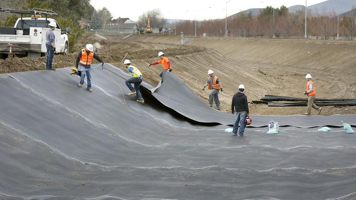 Workers stretch out a layer of liner material Wednesday for the Kennewick Irrigation District canal near the intersection of Creekstone Drive and West 27th Avenue. Inclement weather conditions have put pressure on the crews to finish the project in time for the rapidly approaching irrigation season.