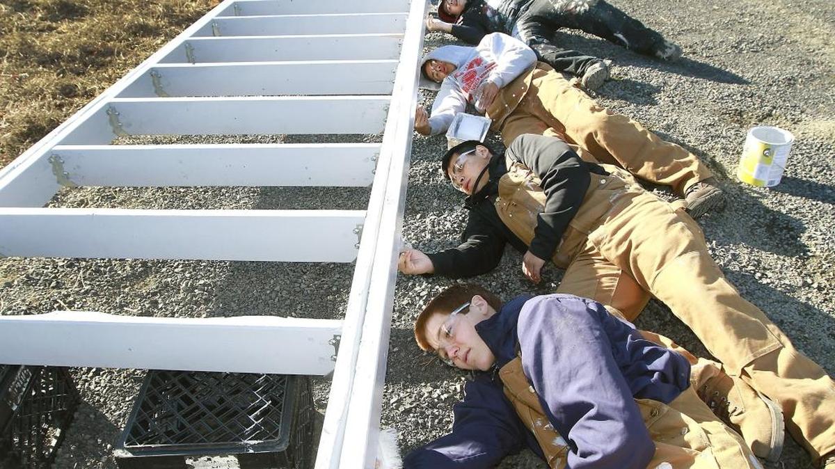 Prosser High juniors Ethan Hurt, Francisco Climaco, Alexis Ramirez, and Julio Ruiz, from bottom, lay down in gravel Monday to paint the underside of a wooden wheelchair ramp support frame. The Tri-Tech Skills Center construction trades students were taking part in a community project with the Rebuilding Mid-Columbia organization of installing the ramp for an elderly couple with limited mobility in the 3300 block of West Payette Avenue in Kennewick. The building materials were paid for by Columbia Valley Daybreak Rotary Club, according to Tri-Tech Skills instructor Tony Milewski.