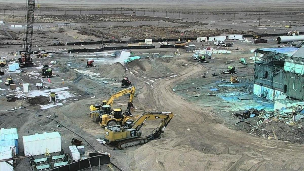Part of the Plutonium Finishing Plant, right, still needs to be demolished. A truck sprays dirt piles of demolition debris. The blue color is from fixative sprayed to prevent radioactive particles from becoming airborne.