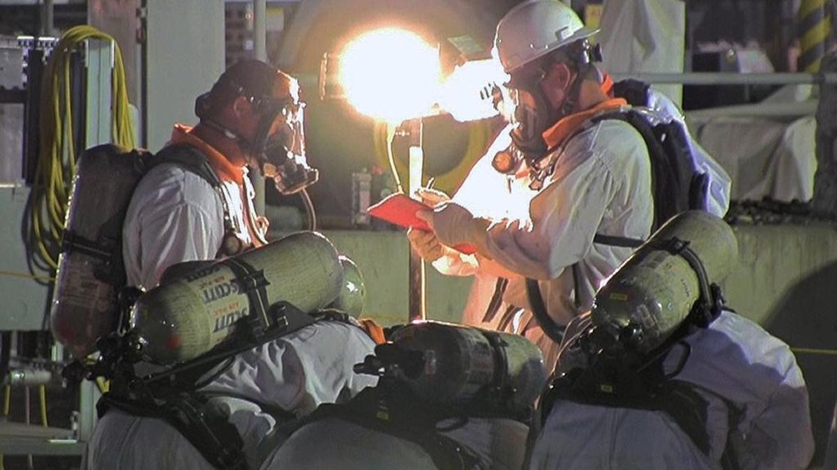 Tank farm workers are shown using supplied air respirators to protect against chemical vapors on a night shift.