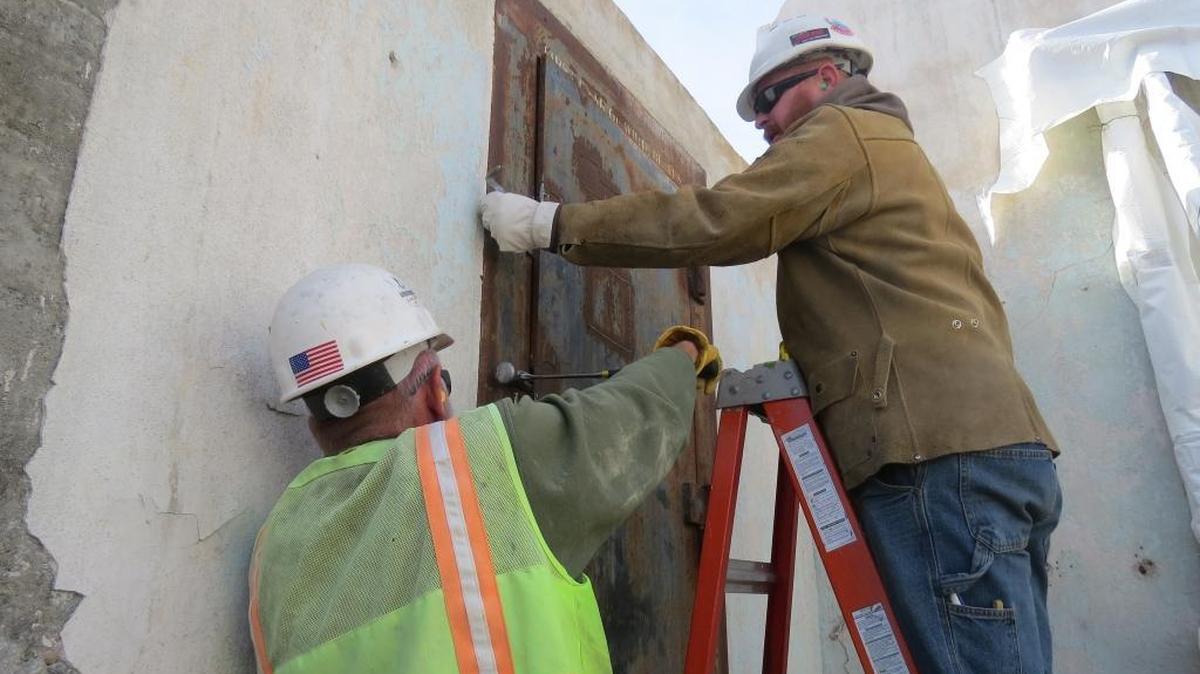 
Michael Warren, top, and Lloyd Hink, both of DGR*Grant, work to loosen the door to the vault at the historic White Bluffs Bank at Hanford.
