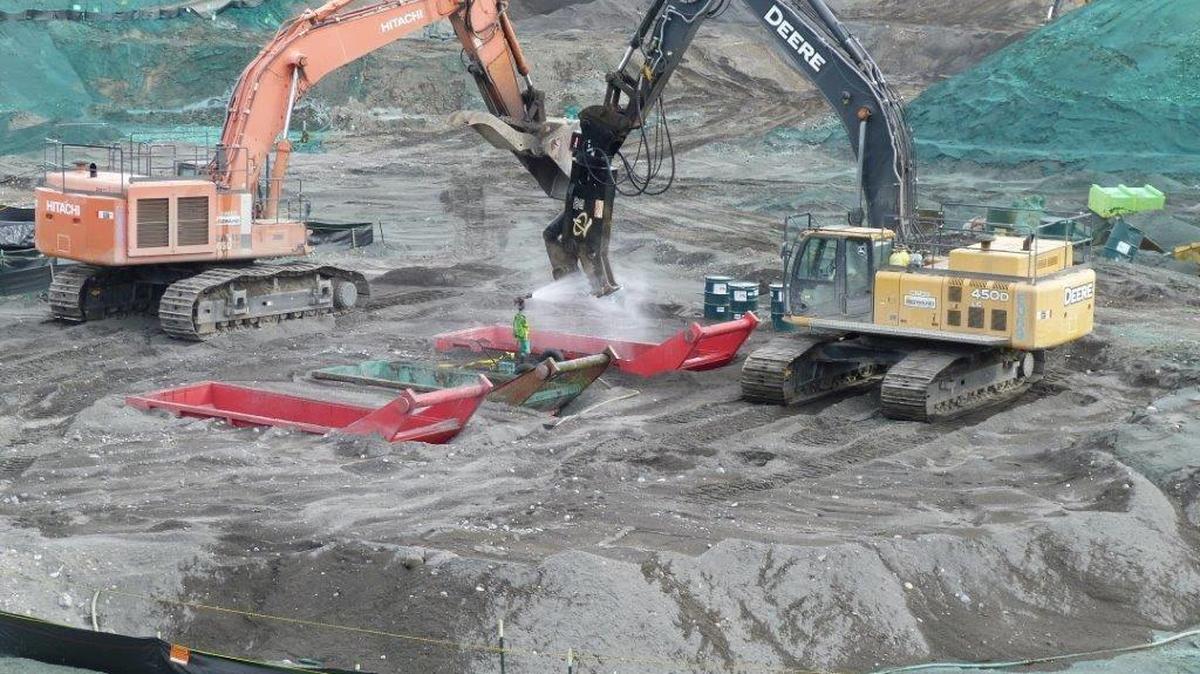 Heavy equipment is used to process drums containing radioactive waste. The drums are munched up in liquid grout within the red boxes partially buried in the 618-10 Burial Ground.