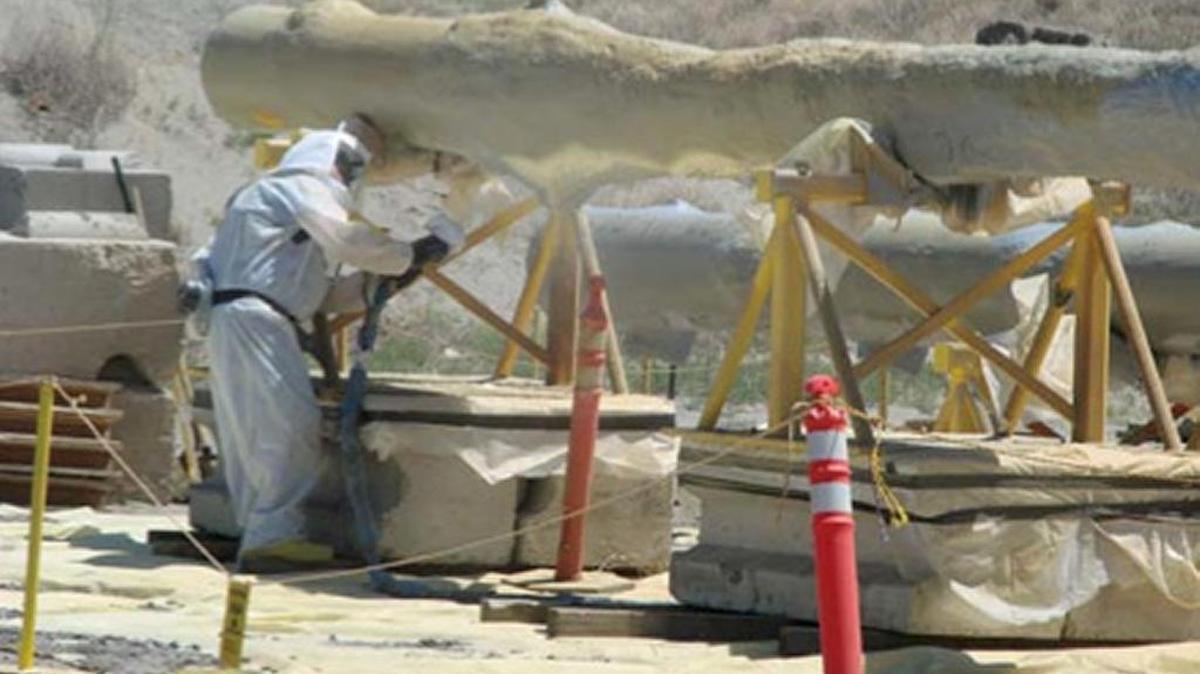 A worker applies a coating of polyurea to a contaminated slurry pump to prepare it to be placed in a Hanford landfill.