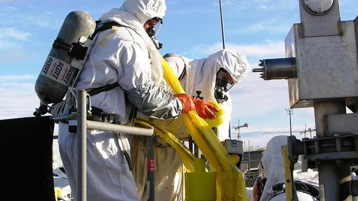 Hanford workers are shown using supplied air respirators and carrying air bottles on their backs within the C Tank Farm.