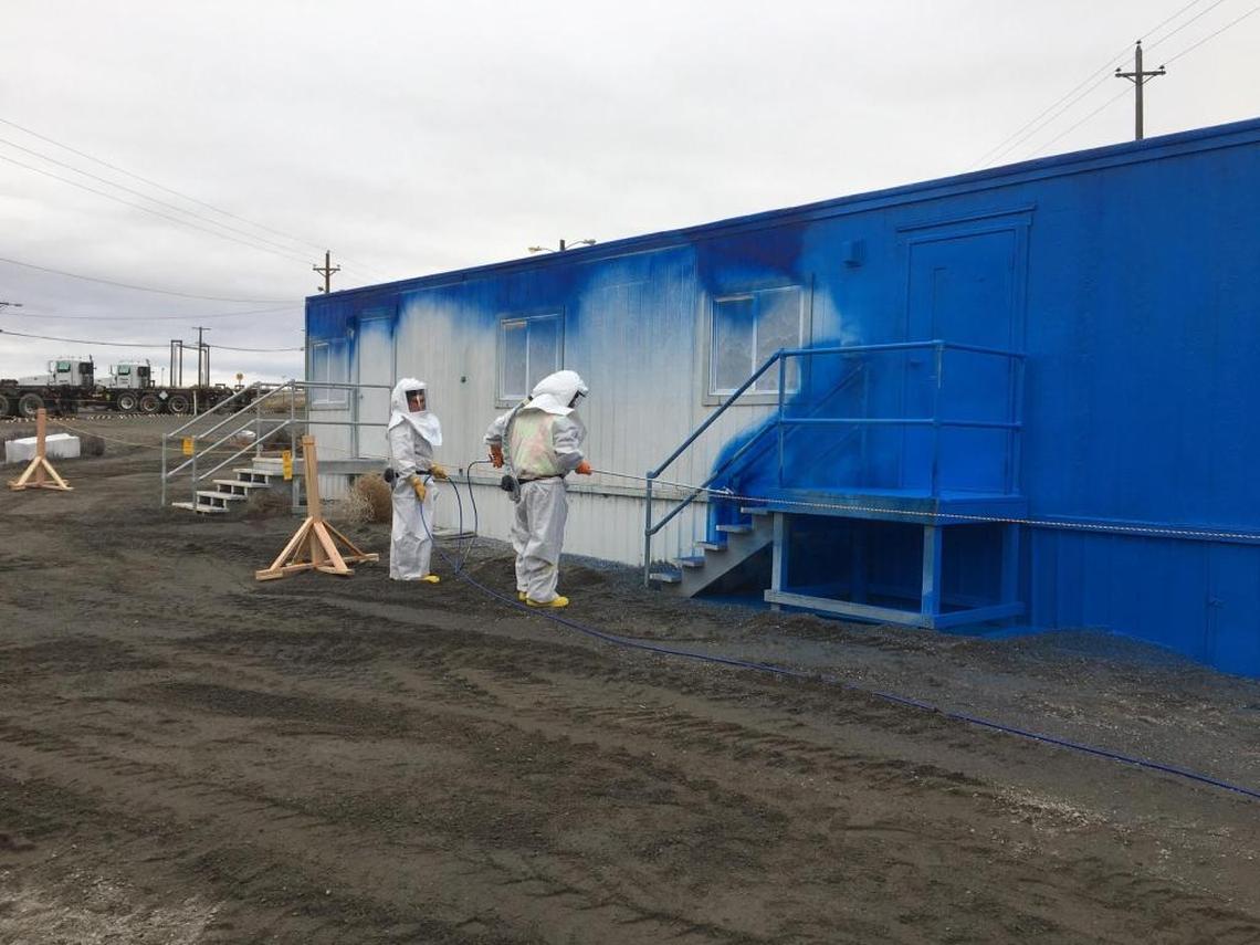 Hanford nuclear reservation workers spray paint-like, blue fixative on a mobile office trailer at the Plutonium Finishing Plant to contain any radioactive contamination on the exterior of the office.