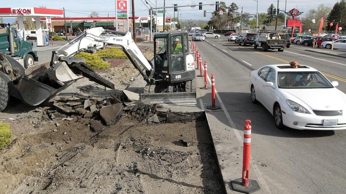 Construction worker Shawn Darling of Granite Construction removes chunks of asphalt Monday from the southbound lane of Edison Street at West Canal Drive as a goggle-wearing dog peers out a sunroof of a passing car. The most recent lane re-configurations are anticipated to last two weeks, according the city of Kennewick. The overall project has caused long-term lane closures between Clearwater Avenue and Canal Drive that are expected to continue until August. The work includes installation of street lights, curbs, gutters, sidewalks, two pedestrian crossings and other upgrades. Access is being maintained to local businesses and apartments.