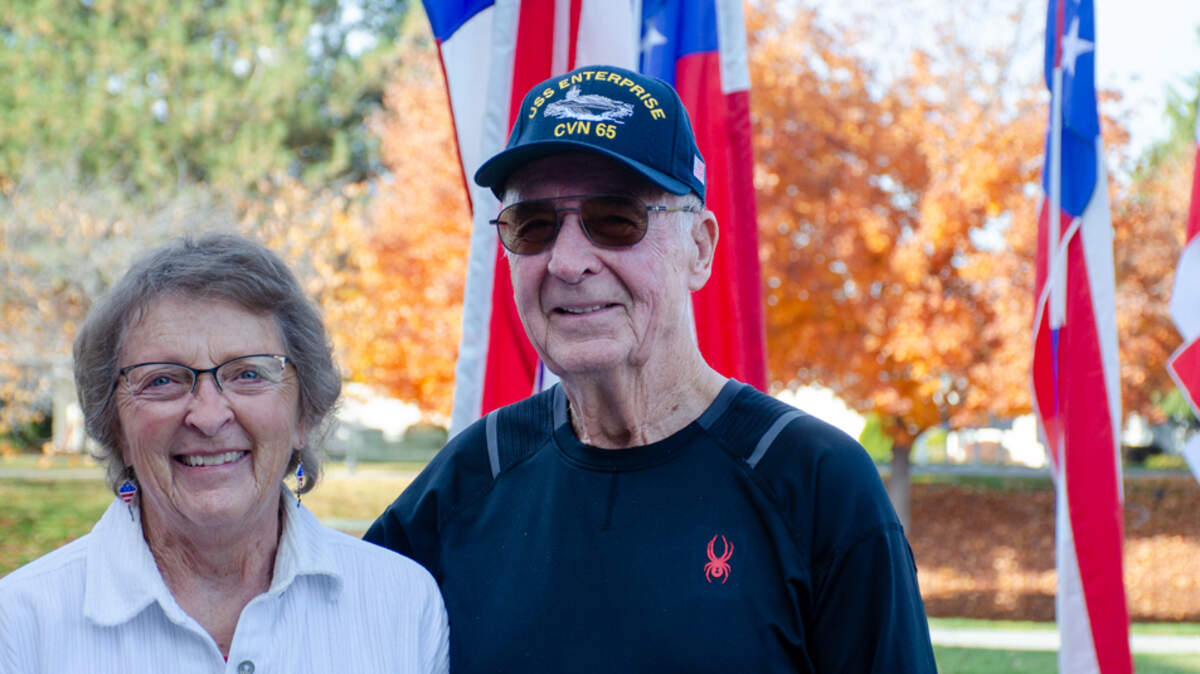 Jim Nett and his wife, Rosa Nett, both 82, pose for a Tuesday photo in front of a gaggle of American flag banners outside Brookdale Canyon Lakes. A retired petty officer who served on the U.S.S. Enterprise during the Vietnam War, Jim Nett erects the banners outside the senior living community during various holidays, including Veterans Day, Memorial Day and Fourth of July.