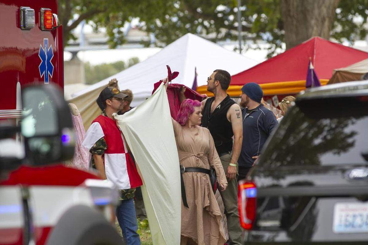 Renaissance festival participants hold up sheets to give first responders and family members privacy after a heavy tree limb fell and killed a woman.
