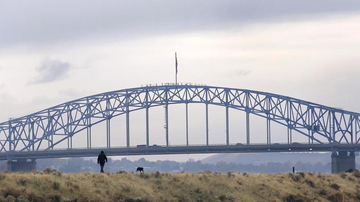 Grey clouds dominate the sky Monday morning as an owner and dog make their way along the Sacagawea Heritage Trail in Pasco just downriver of the blue bridge. Breezy conditions are expected through Tuesday, but gloomy skies might last through most of the week, according to the National Weather Service. See weather, Page 18A.