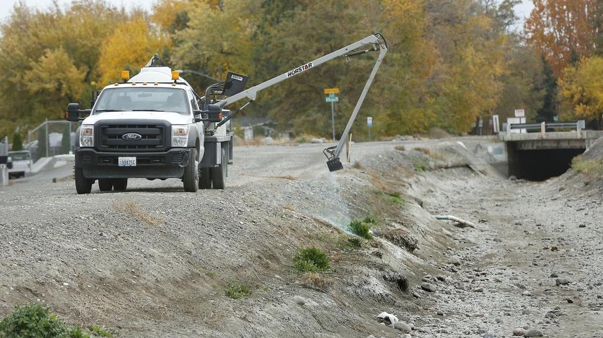 Kevin Walters uses a remote-controlled hydraulic spray arm on a Columbia Irrigation District truck to spray a herbicide Tuesday on the bank of the district’s main canal in Kennewick along West Canal Drive near North Lyle Street. Walters said the spray helps reduce weeds during the off-season.