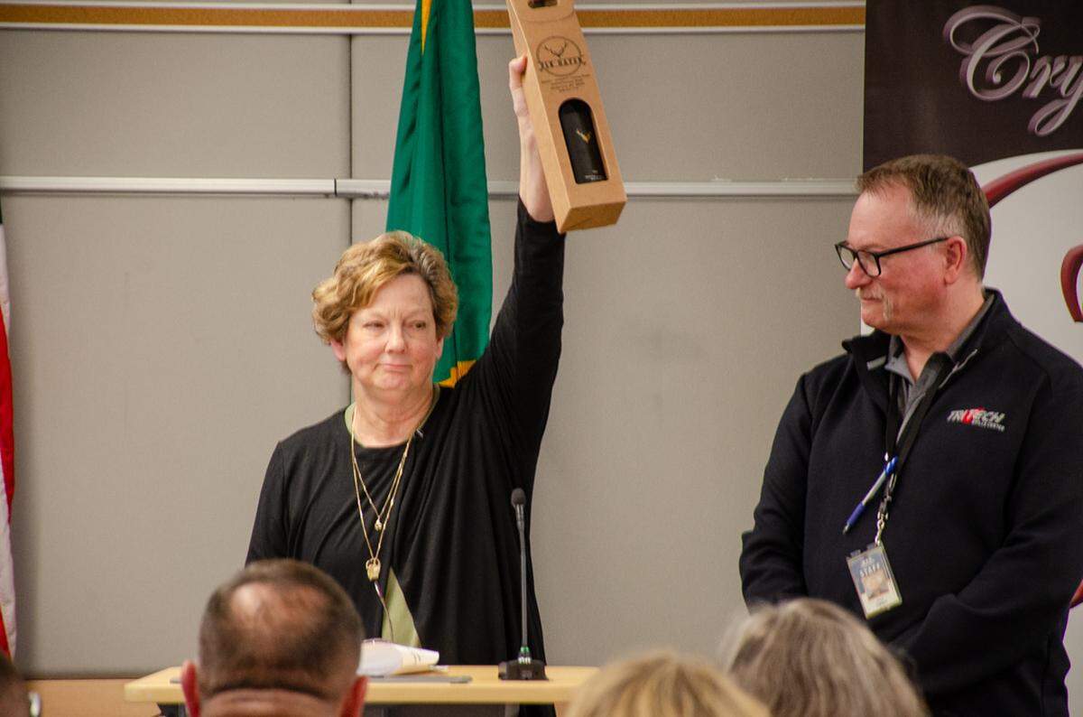 ESD 123 Board Member Teri Kessie lifts a bottle of wine in commemoration of Gerry Ringwood, a lifelong advocate and educator of career and technical education. It’s the Crystal Apple Awards’s first posthumous special recognition. He died in February 2025.