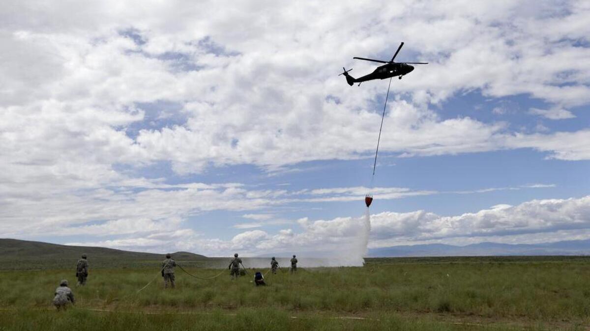 Washington National Guard members watch as a fire fighting helicopter drops water nearby during training for wildfires at the Yakima Training Center in 2013.