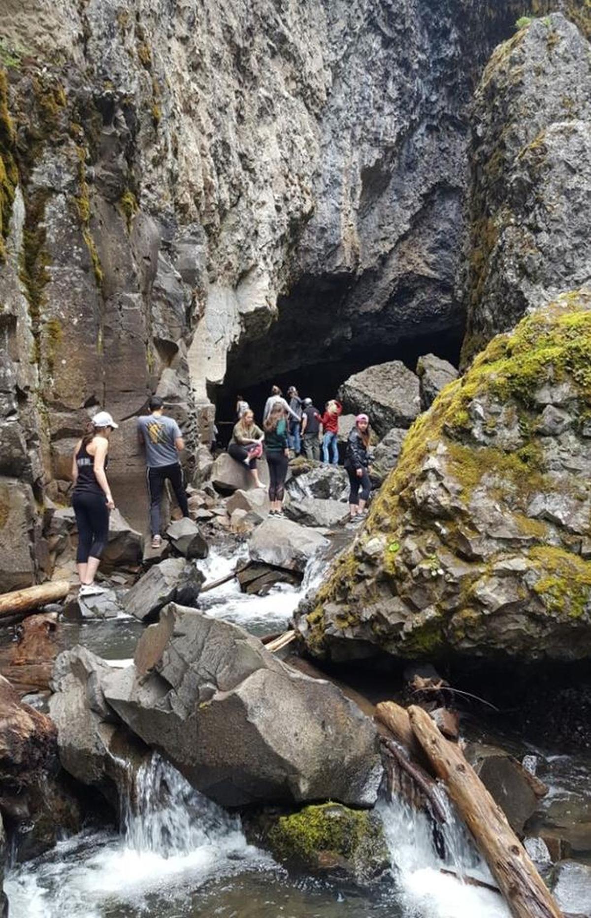 Hikes scramble across logs and boulders along Devil’s Creek at the exit to the younger cave.