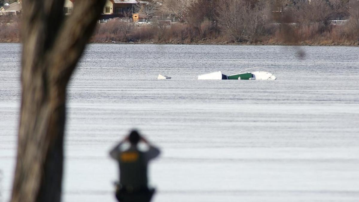 Deputy JP Benitez, of the Benton County Sheriff's Office, uses binoculars Monday to look at a partially submerged boat floating down the Columbia River near Columbia Park in Kennewick.