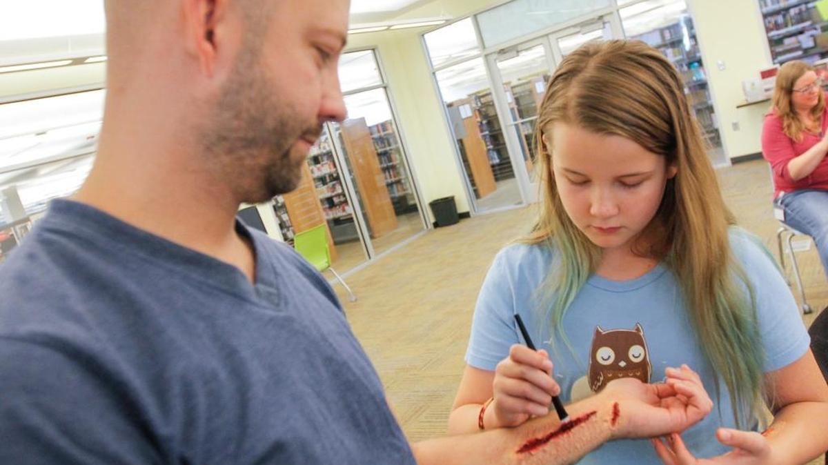 Josh Aldous of Richland watches his daughter, Bella Aldous, paint red makeup on a fake wound they created Saturday during Monster Makeup: Walking Wounded at the Richland Library.