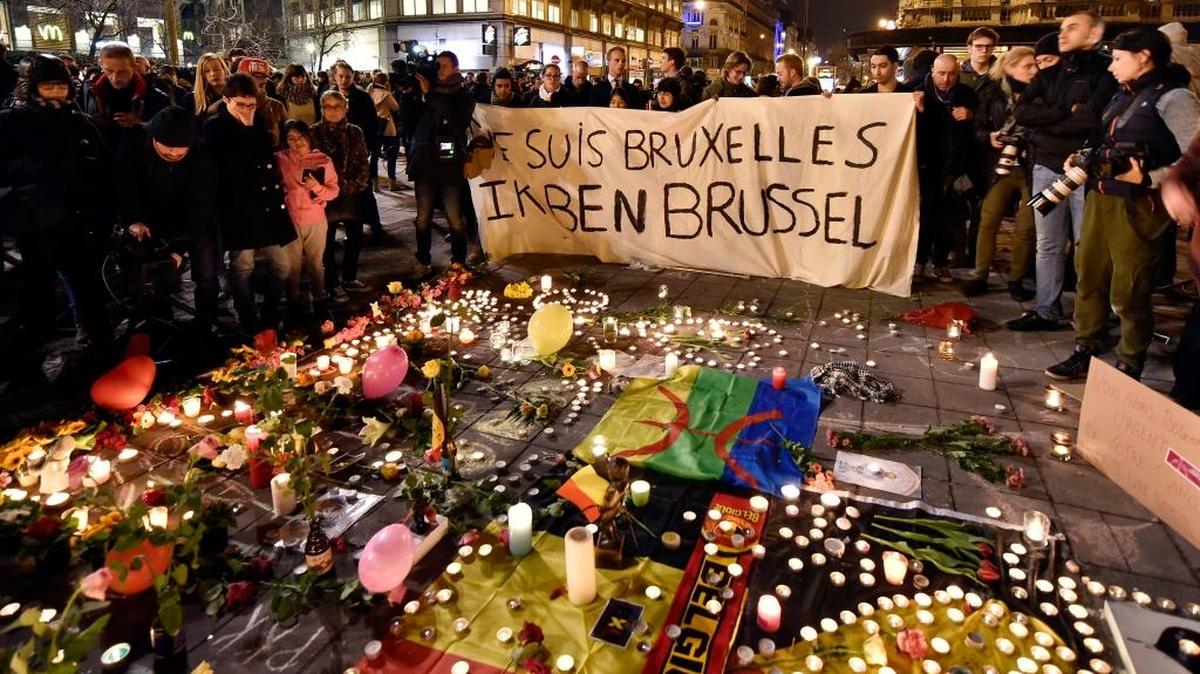 People holding a banner reading “I am Brussels” behind flowers and candles mourn for the victims Tuesday at Place de la Bourse in the center of Brussels. Bombs exploded at the Brussels airport and one of the city’s metro stations, killing and wounding scores of people, as a European capital was again locked down amid heightened security threats.