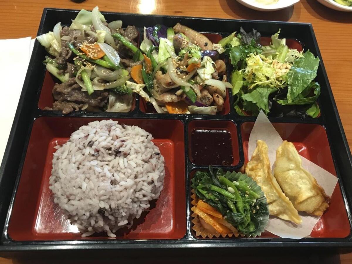 This lunch speacial at Gangnam Style Korean BBQ consists of a bento box that is populated with rice, bul go gi, dumplings, spinach and salad.