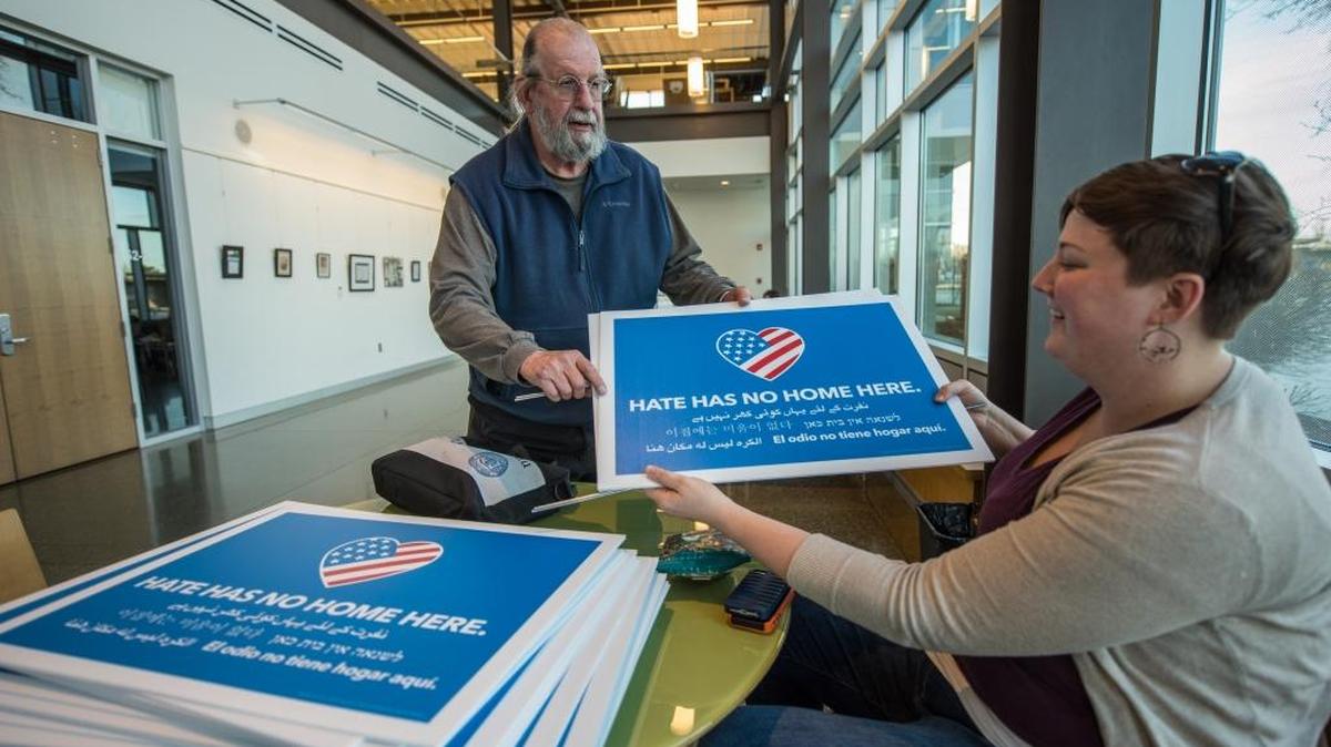 Chuck Eaton of Richland picks up a “Hate has no home here” sign from Ellen McBriarty of the Love, Not Hate Tri-Cities group at the Richland Public Library on Thursday evening.