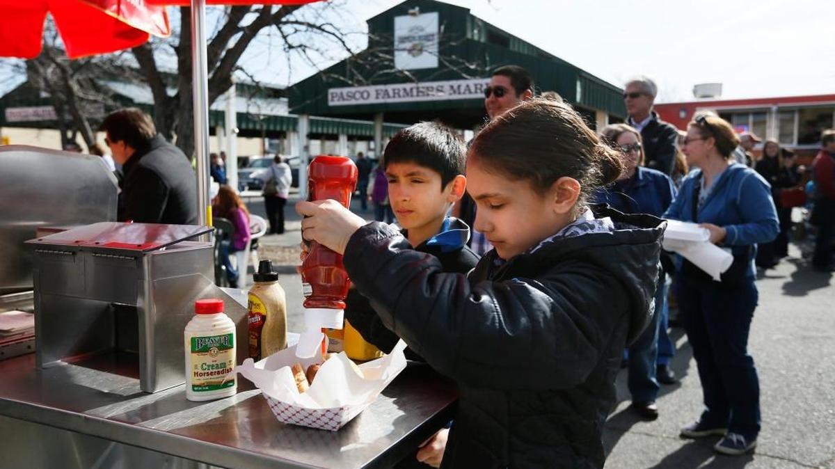 Trinity Figueroa Romero, 10, puts ketchup on her hot dog as her brother Dean Figueroa Romero, 9, waits for his lunch to be delivered in this file photo from the debut of Food Truck Friday at the Pasco Farmers Market.