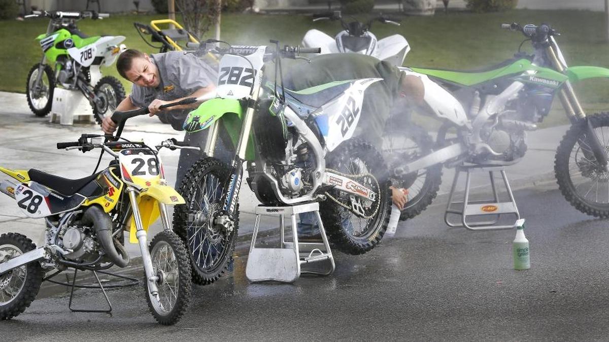 Dustin Raymond, left, and Matt Starkey pressure wash and scrub the dirt off their two families’ motorcycles and ATVs Monday after spending a weekend of recreational riding. They also ride competitively at the moto-cross course at the Richland ORV Park. The duo were working in front of Raymond’s home on Kona Drive in West Richland.
