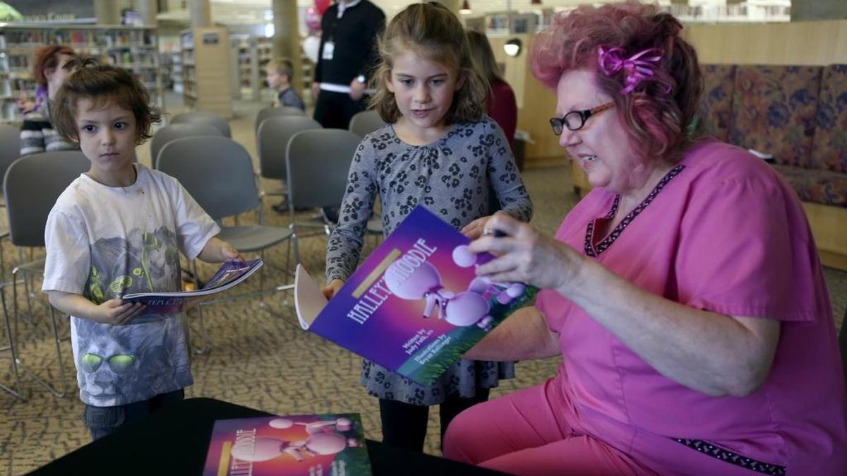Author Judy Folk, a nurse at Trios Health in Kennewick, signs a copy of her newest children’s book Halley’s Hoodie for Olivia Johnson, center, as Rawley Weedmark looks on. The signing was during a book reading Tuesday at the Mid-Columbia Library in Kennewick. Folk wrote the book, which focuses on the challenge of coping with a cancer diagnosis, to make cancer a little less scary for school-aged children. See a video at www.tricityherald.com/video.