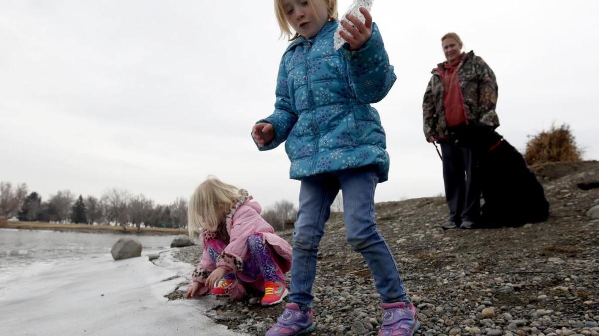 Sisters JoLynn, left, 5, and Braelynn Santens, 3, throw ice at the Family Fishing Pond on Wednesday as their mother Sarah and dog Tucker look on at Columbia Park in Kennewick. Mark Allen of Allen Water Rescue Services warns that the thin ice is thawing and children should always be supervised near the water. “No ice is safe ice,” he said.
