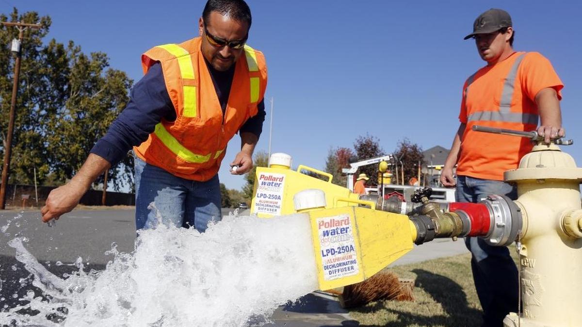 Joe Garcia, center, city of Pasco employee, takes a sample of water as co-worker Brock Allen looks on while flushing water lines on Road 108 in Pasco last year.